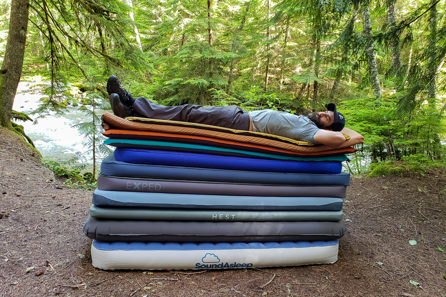 A man laying on top of a huge stack of camping mattresses