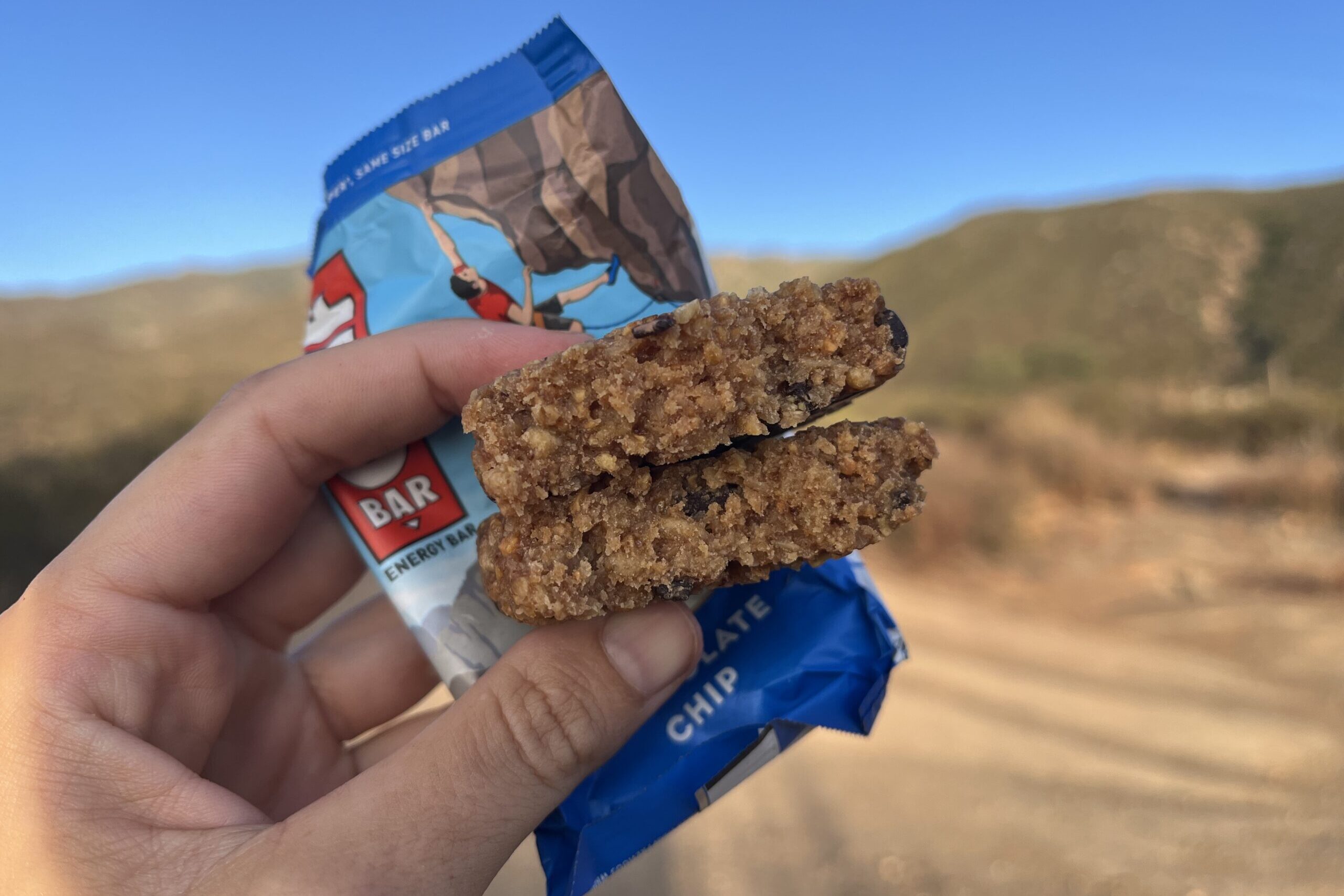 hand holding up Clif Bar in a mountainous setting