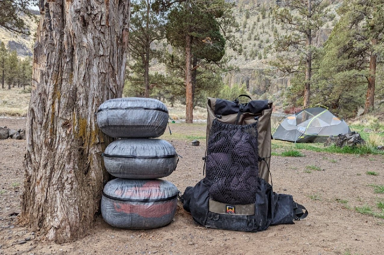 three hyperlite mountain gear pods stuffed and zipped next to an empty backpack in a campsite