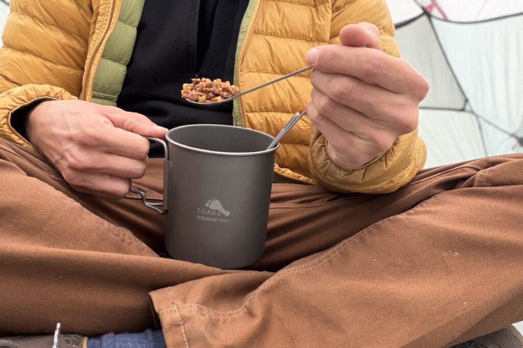 a chest down view of a hiker scooping a bite of food from a titanium pot