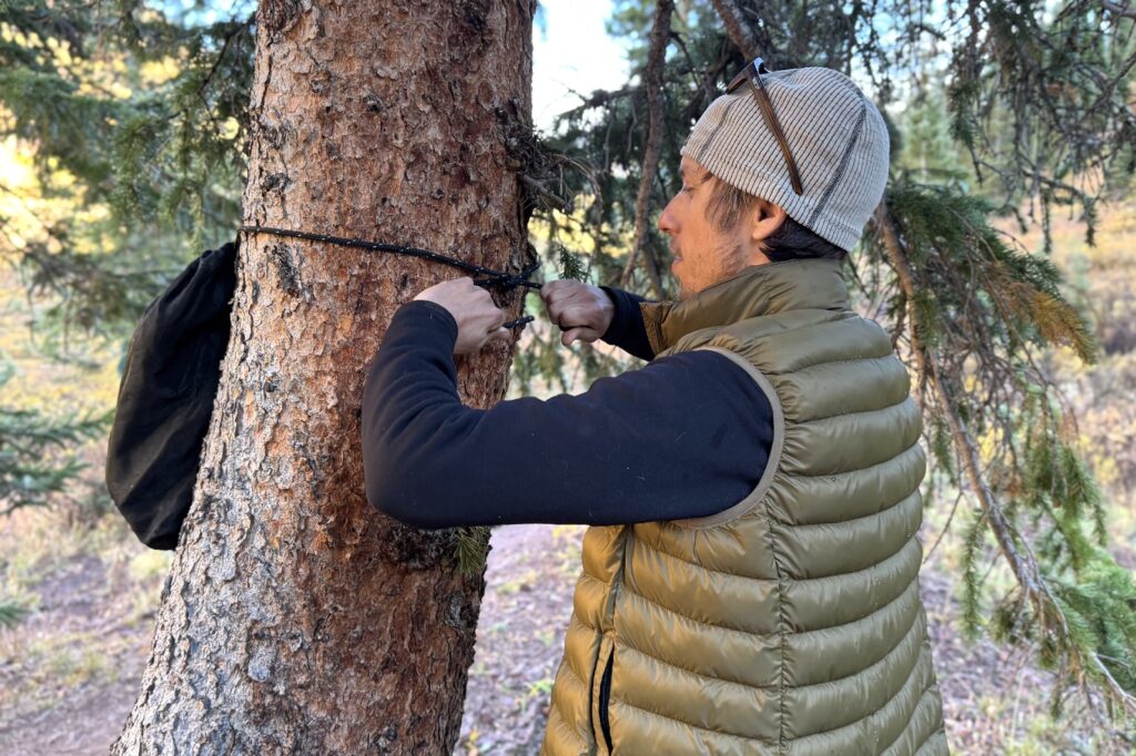 a hiker ties an ursack around a tree trunk