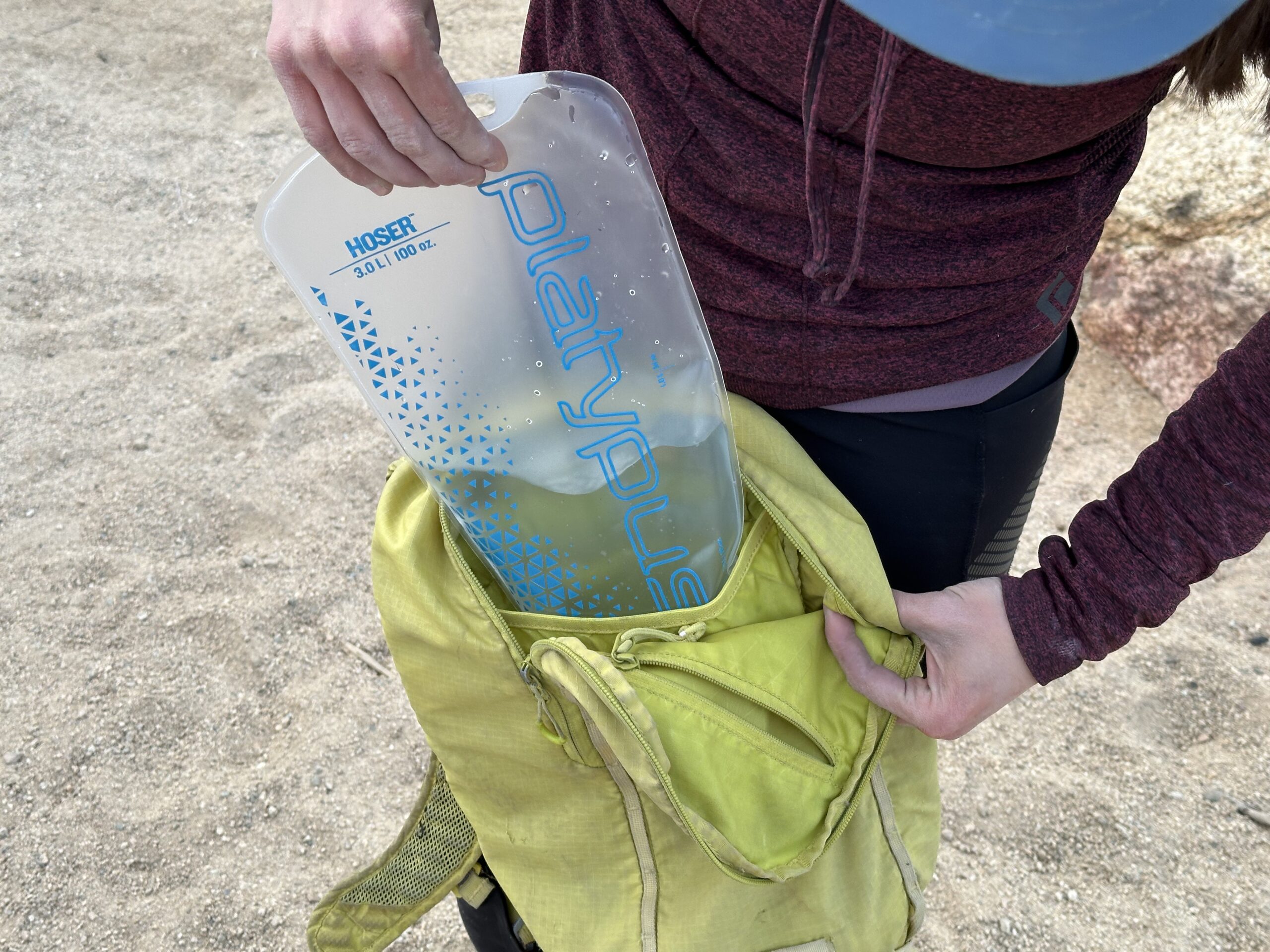 Close up of a hiker loading the Platypus Hoser into the hydration sleeve of a small yellow day pack