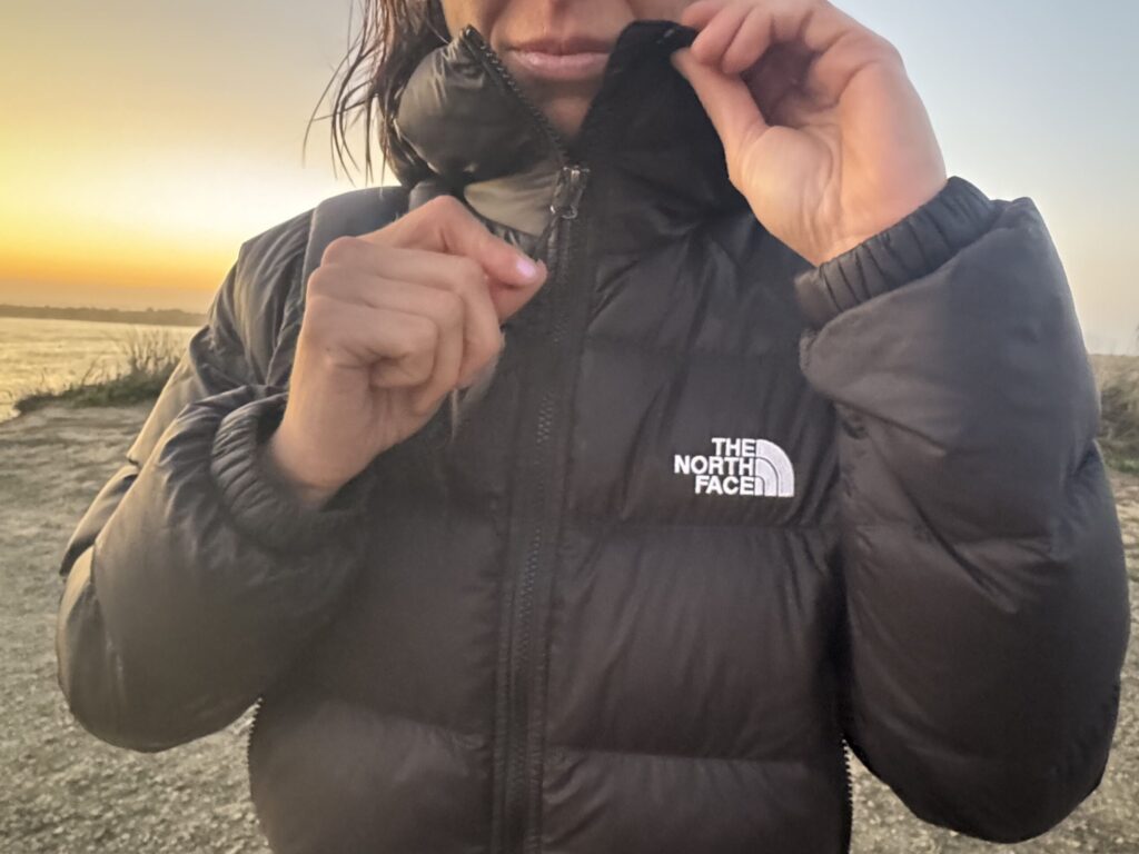close up of a woman at sunset unzipping a north face hydrenalite down hoodie