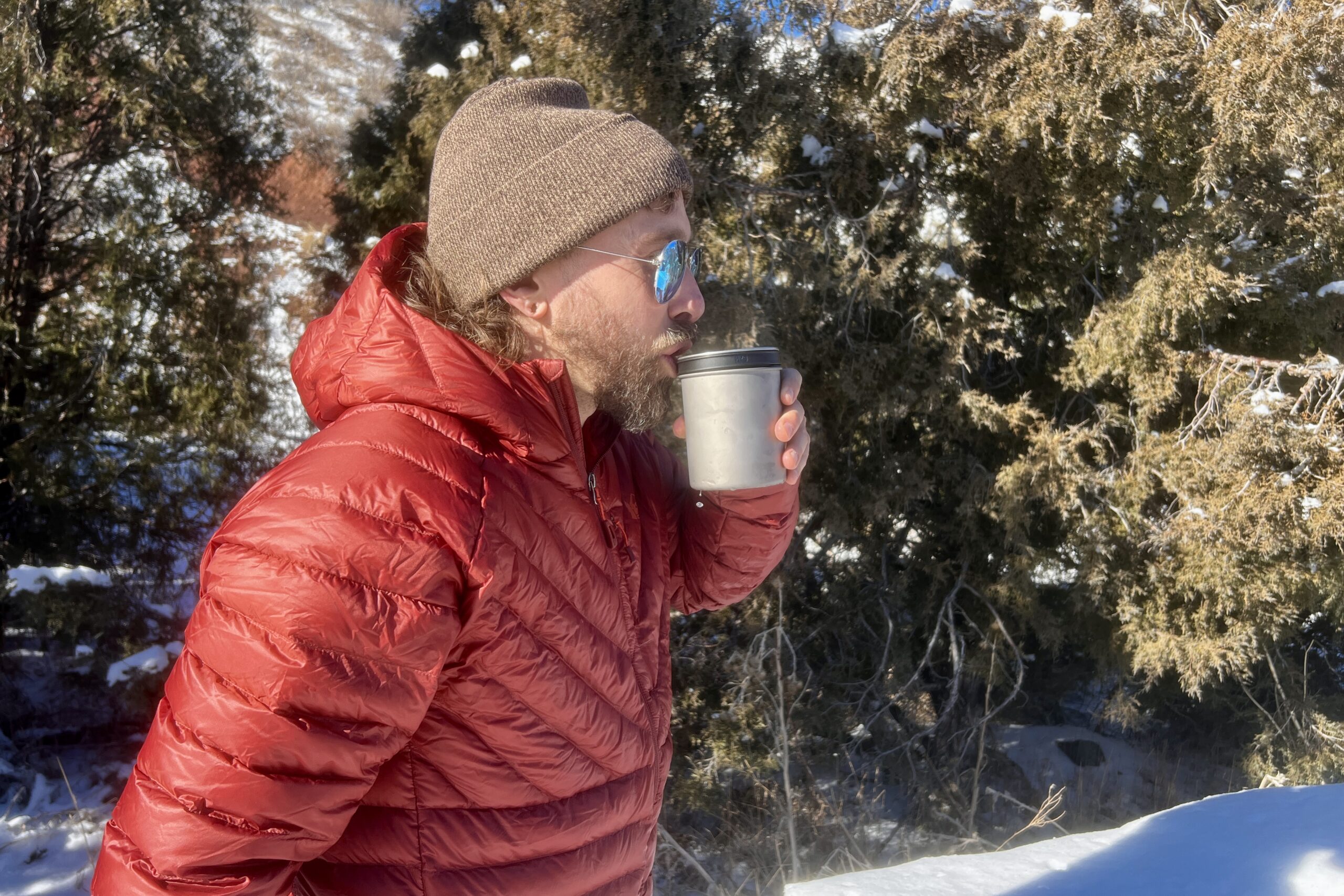 A hiker sips from the insulated mug of the thermostack combo with a snowy desert background.