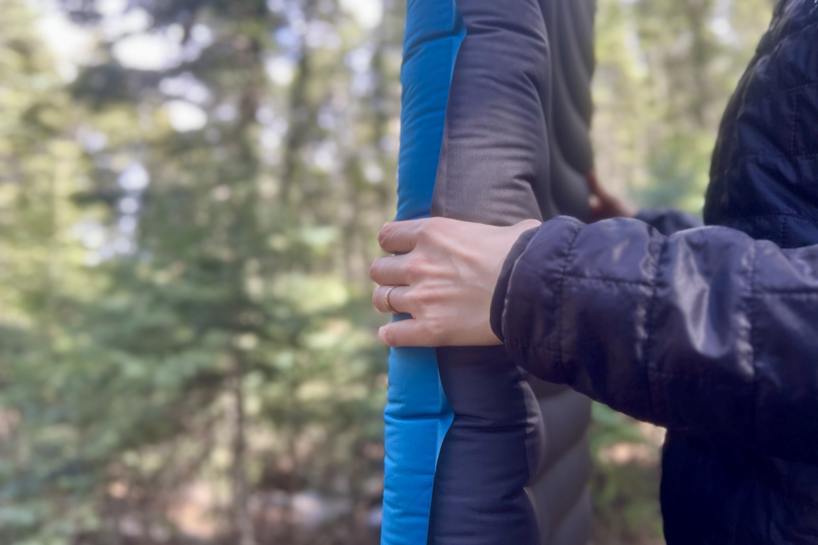 a close up of a hiker grasping the thickness of a blue sleeping pad