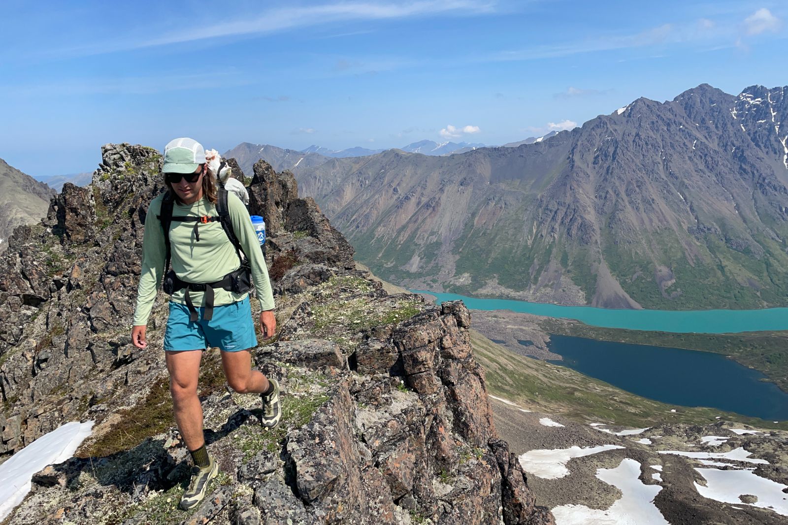 A man walks along a ridgeline above an alpine lake.