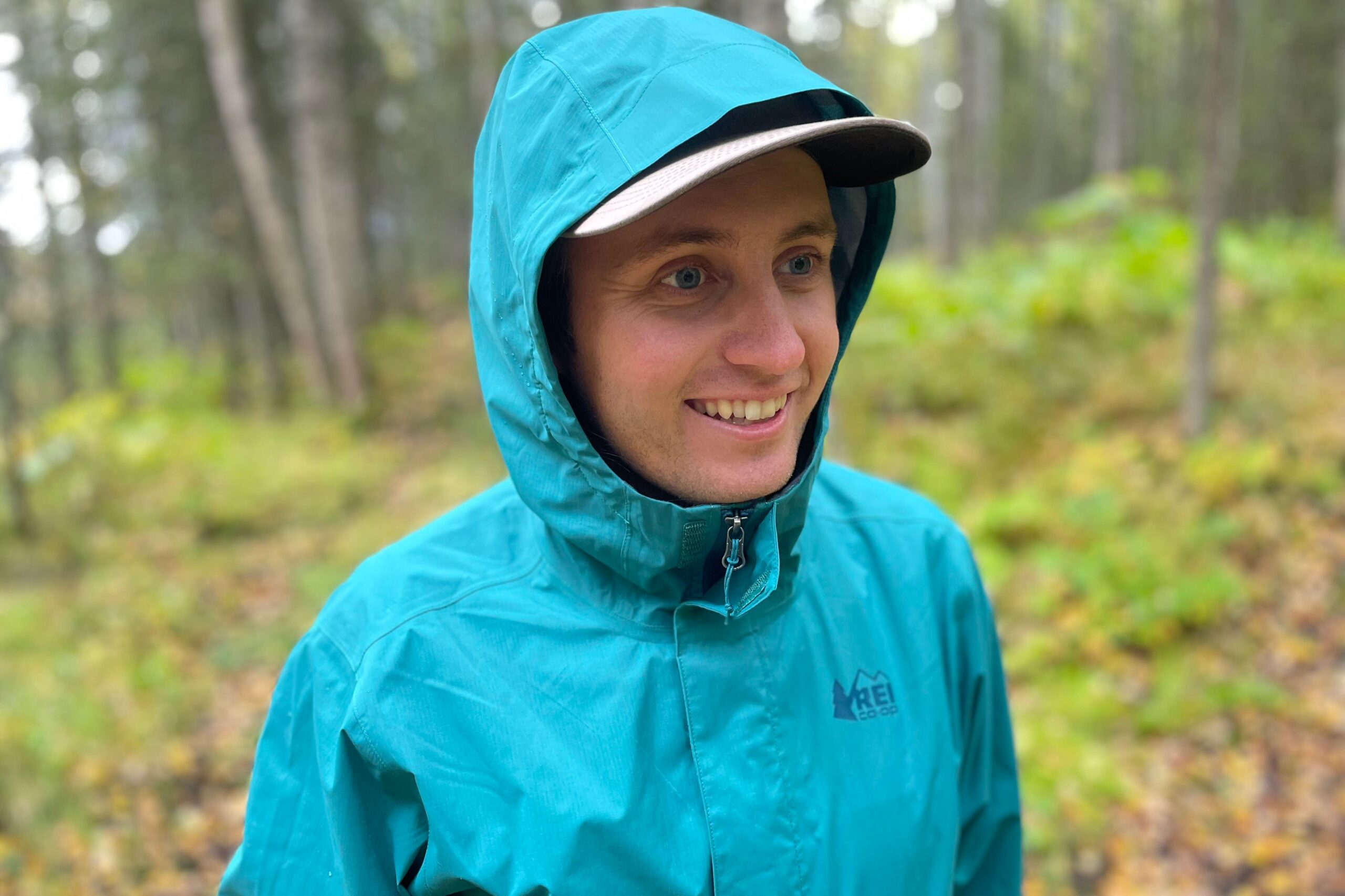 A man smiles while wearing a hooded rain jacket.