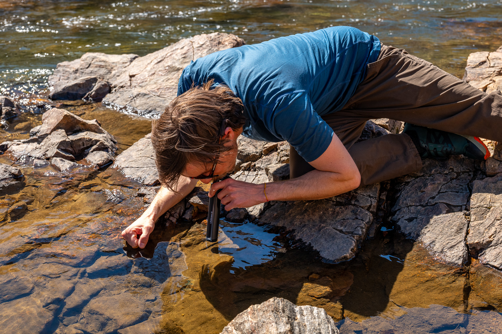 a hiker sips water straight out of a creek with the peak straw