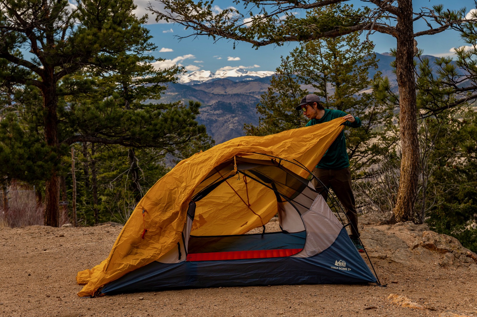 a hiker pulls a yellow rainfly over a tent