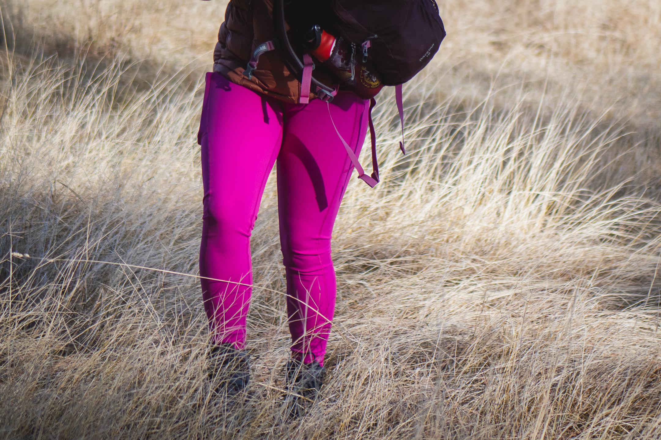 Person hiking in bright pink leggings, wearing a bronze down jacket and black gloves.