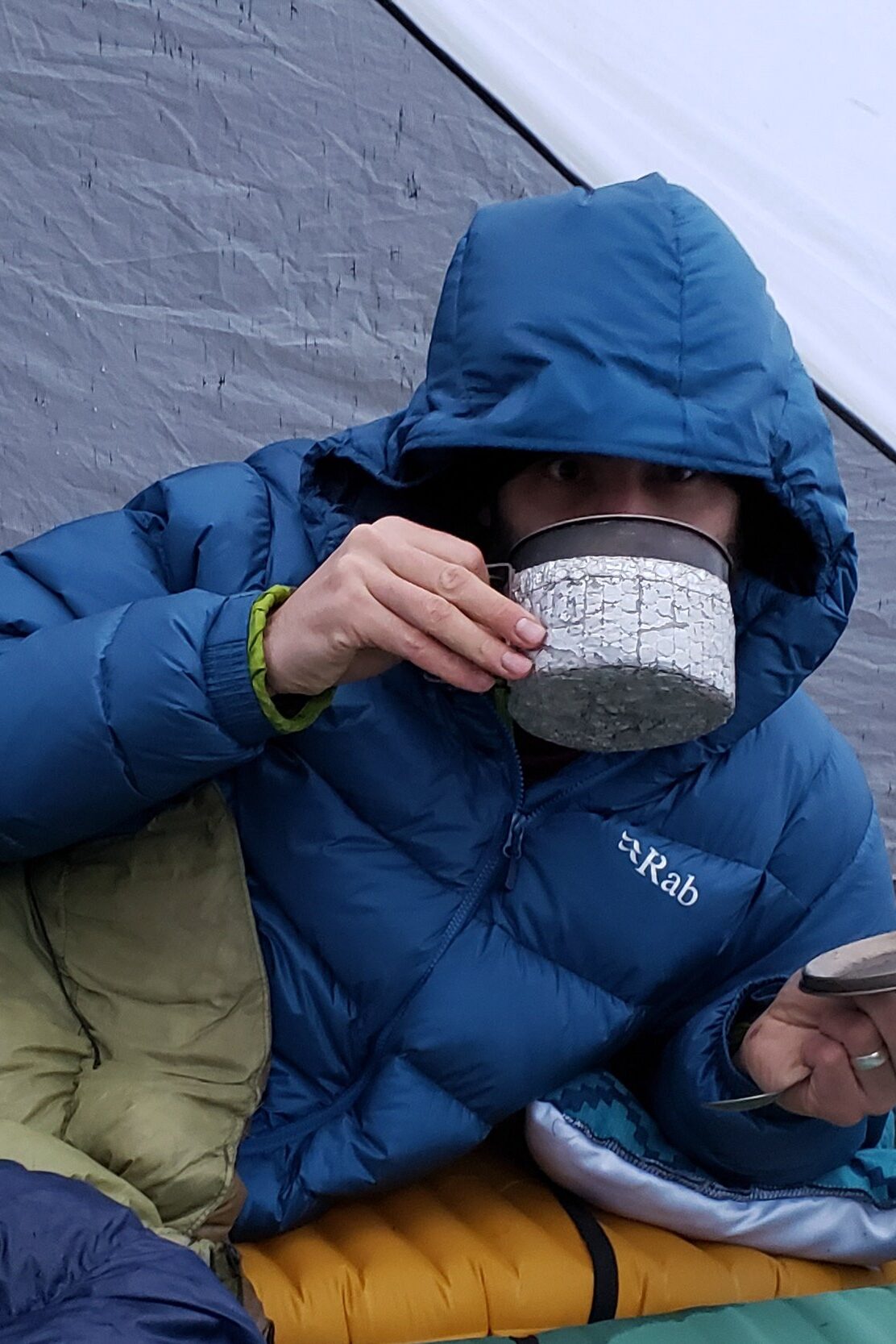 a man wearing the rab neutrino pro while drinking camp coffee