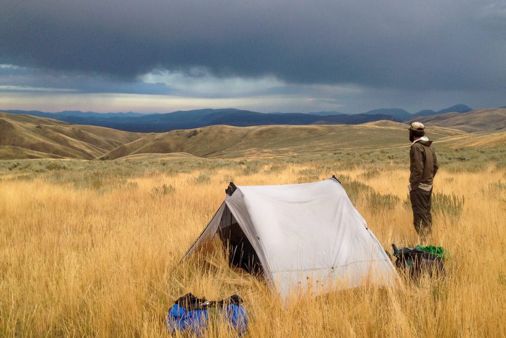a man looks at an approaching storm over a wide high grass prairie